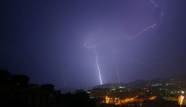 3 lightning photos shot from the same viewpoint.  Same landscape, choice of bolts.  The image is taken from a high viewpoint, overlooking trees, a town and mountains.  This is my favourite of the 3 because of the almost 'batman'-like lighting and colour