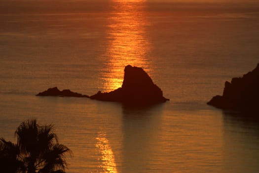 An almost impressionist view of a rock at sea backlit by the reflection of the setting sun.