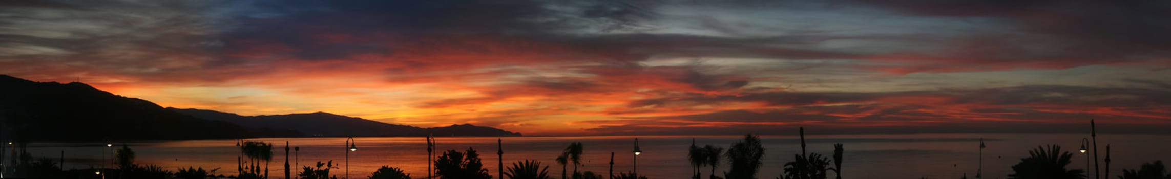 A very wide panoramic image showing a pretty and spectacular sunrise over sea and mountains
