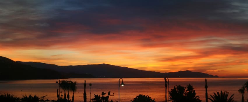 A very wide panoramic image showing a pretty and spectacular sunrise over sea and mountains