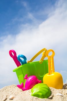 Child's bucket, spade and other toys on tropical beach against blue sky