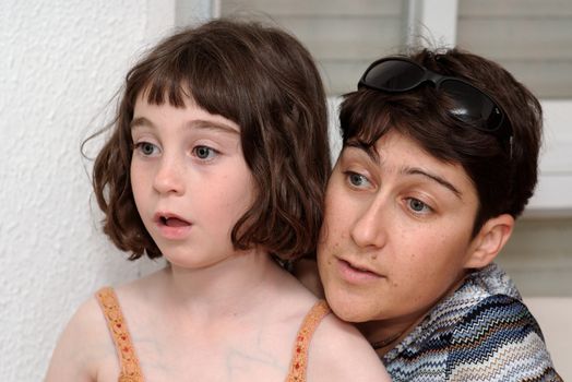 Mother and cute little daugher watch TV in great concentration