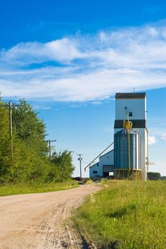 A prairie grain elevator with a dirt road running to it shot on a partly cloudy day
