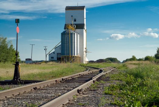 Prairie railroad tracks running along beside a tall grain elevator and vanishing in the distance