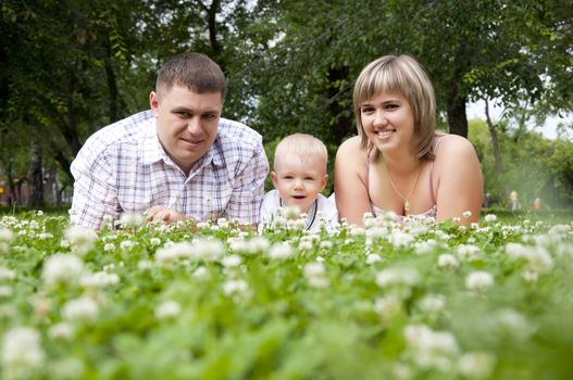The young family in park, lays on a grass and smiles