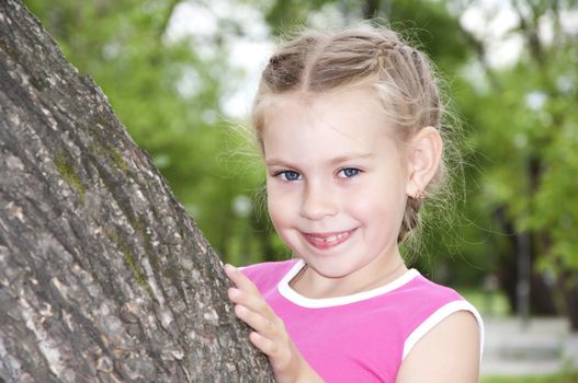 portrait young girl peeping out tree, in summer park