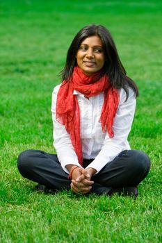 Pretty young indian girl sitting on the grass at a park