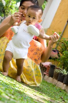 cute asian baby girl learning to walk assisted by her mother