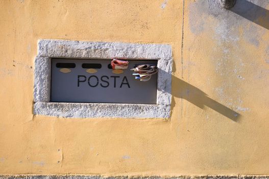 Italian mailbox in yellow wall with newspapers