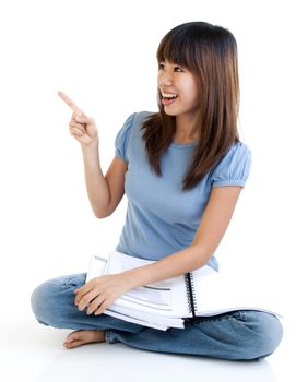 Asian student sitting on floor, pointing to empty space, ready for text.