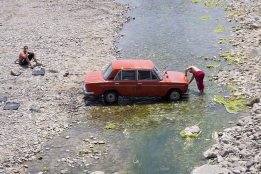 Man washing car in river in Armenia. Summer day