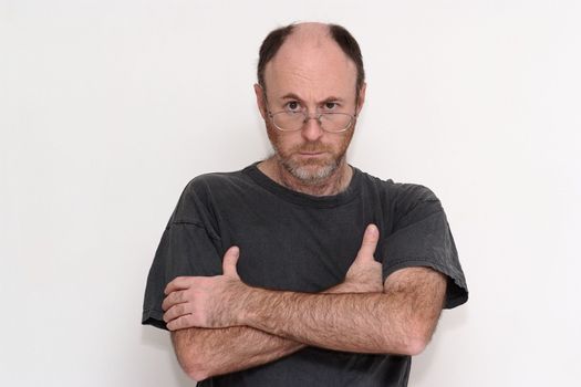 Unshaved disheveled man in spectacles frowning sullenly towards the camera