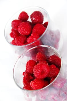 two portions of appetizing red fresh ripe raspberries in glasses over white