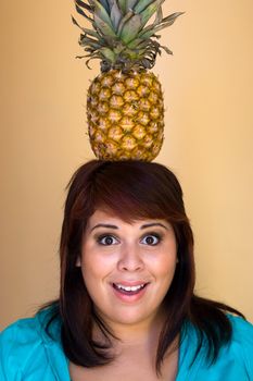 A young woman with a funny expression balancing a pineapple on her head.