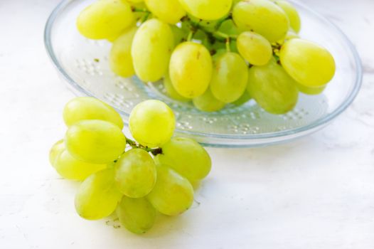 Green ripe grapes in plate on light background