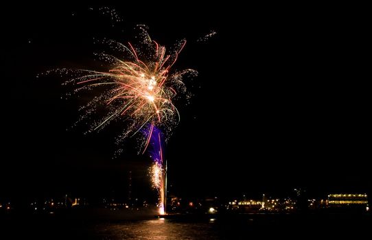 Fireworks from boat on the river with night lights of the city in background