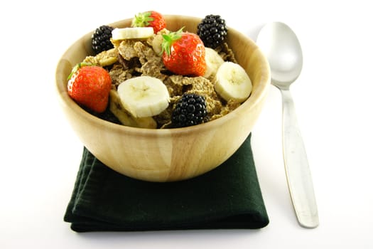 Crunchy delicious looking bran flakes and juicy fruit in a wooden bowl with a spoon and a black napkin on a white background