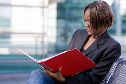 African american business woman reading documents in a folder in front of an office building