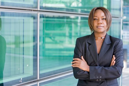 Black african american business woman posing in front of a modern office building with arms folded