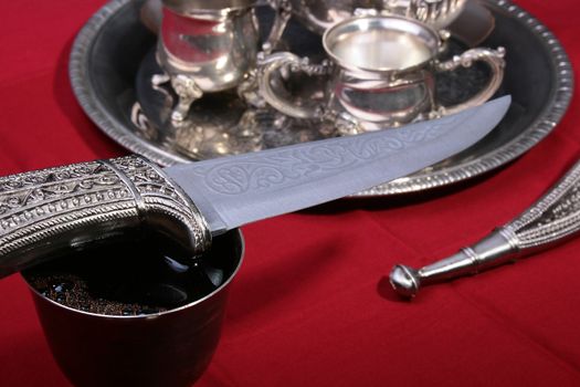 Dagger and silver glass with wine on a red background.