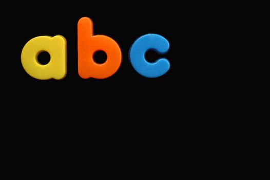 The letters a, b and c from a child's toy alphabet set, placed on a black background. Space for text elsewhere in the image.