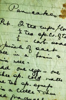 Close-up of a hand-written recipe for pancakes, on stained and crumpled paper. Found in a 100-year old cookery book.
