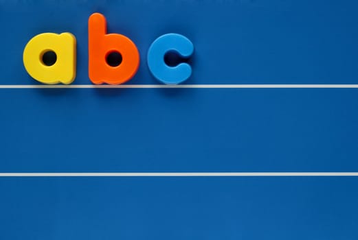 The letters a, b and c from a child's toy alphabet set, placed on a blue, lined background. Space for text elsewhere in the image.