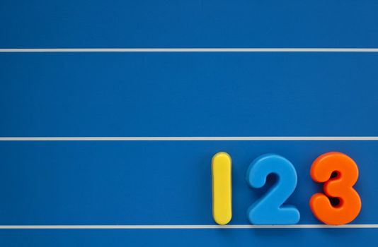 The numbers 1, 2 and 3 from a child's toy alphabet set, placed on a blue, lined background. Space for text elsewhere in the image.