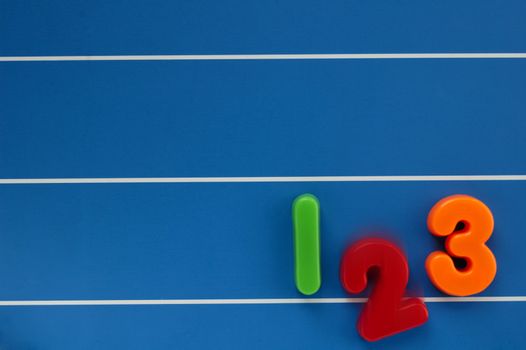 The numbers 1, 2 and 3 from a child's toy learning set, on a blue, lined background. The number 2 dropping out of the line, with motion blur.