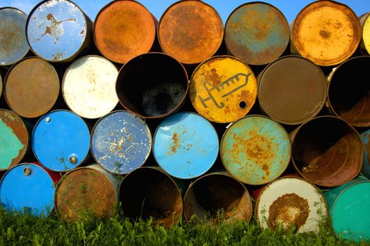 A stack of old oil drums at a music festival, ready to be set out as rubbish bins. One of them is for used syringes. Blue sky above and behind, green grass below.