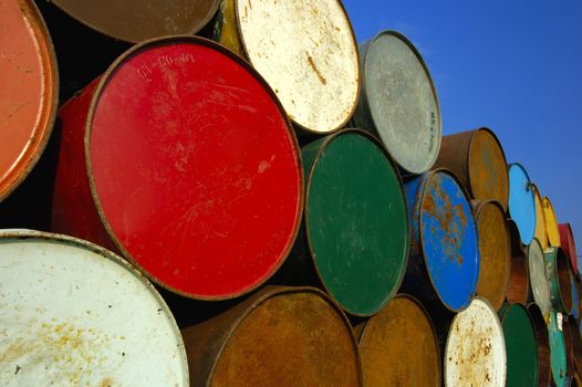A stack of multi-coloured oil barrels, towering in to the clear blue sky. Space for text in the sky.