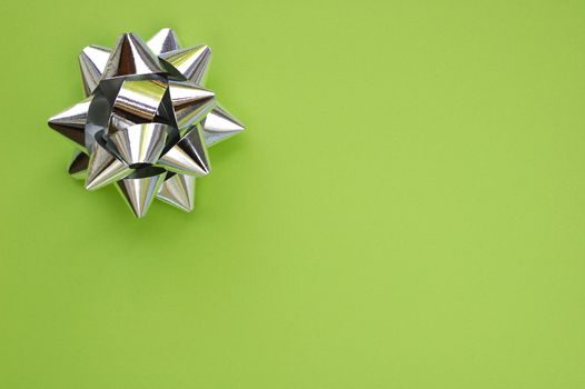 A decorative star, made from silver ribbon, on a plain green background with space for text (copy).