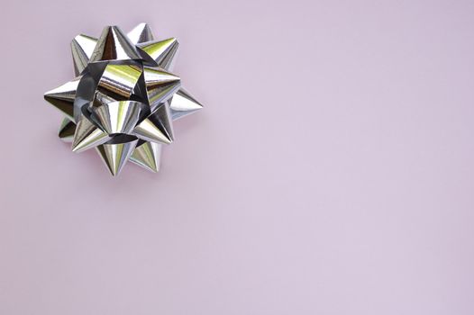 A decorative star, made from silver ribbon, on a plain lilac background with space for text (copy).
