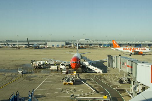 A Norwegian Air Shuttle airplane gets maintenance and refueling before accepting new passengers at London Stansted Airport. Easyjet is in the background, off to departure.