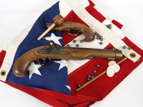 Two antique muzzel loader guns displayed over a US flag. Over a white background.