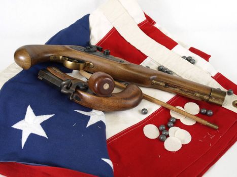 Two antique muzzel loader guns displayed over a US flag. Over a white background.
