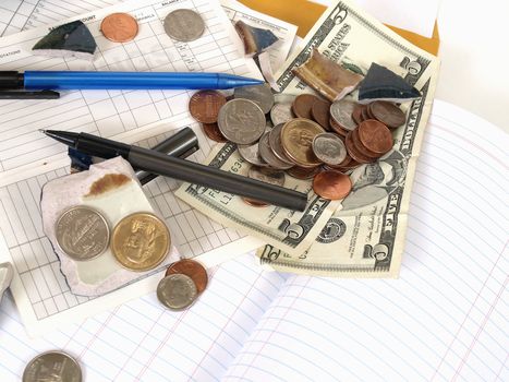 US Currency and broken ceramic pieces from a bank lay over empty ledger books. 