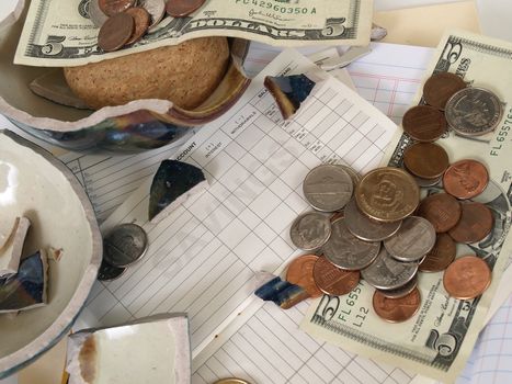 US Currency and broken ceramic pieces from a bank lay over empty ledger books.