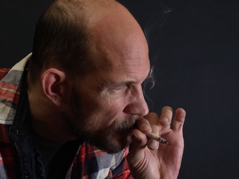 A man in a plaid shirt smokes a cigarette over a black background.