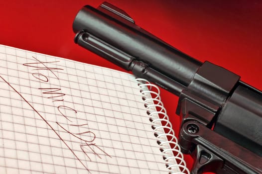 Close-up of a notepad with word 'homicide' and gun on red background with selctive focus