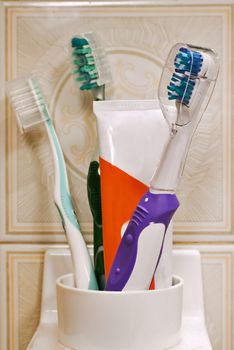 Three toothbrushes and toothpaste in plastic glass