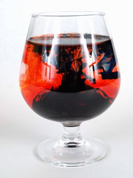 Abstract image of crosses reflecting on a red and black swirled background inside a brandy glass. Over white.