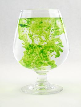 A liquid filled glass with green swirls over a white background.