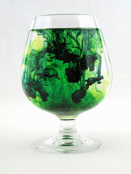 A liquid filled glass with green swirls over a white background.