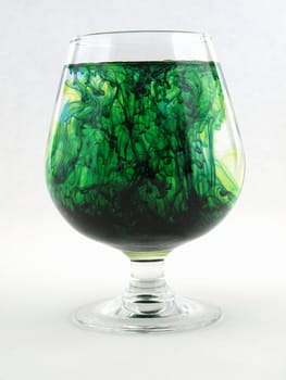 A liquid filled glass with green swirls over a white background.