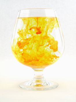 A liquid filled glass with yellow swirls over a white background.