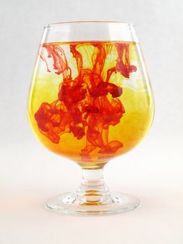 A liquid filled glass with red and yellow swirls over a white background.