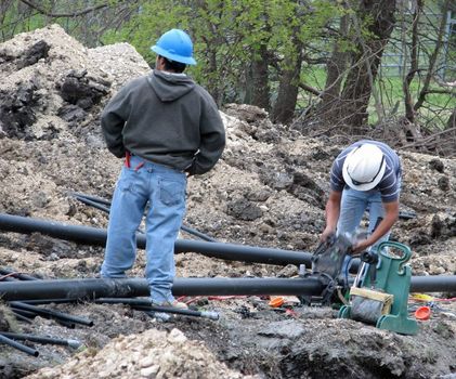 Construction workers cut a large pipe to be used as conduit for underground electrical lines.