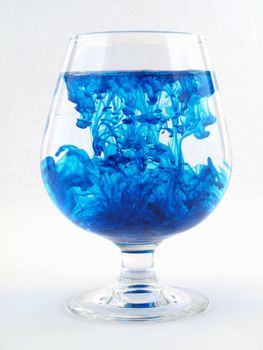 A liquid filled glass with blue swirls over a white background.