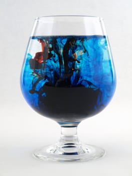 A liquid filled glass with red and blue swirls over a white background.